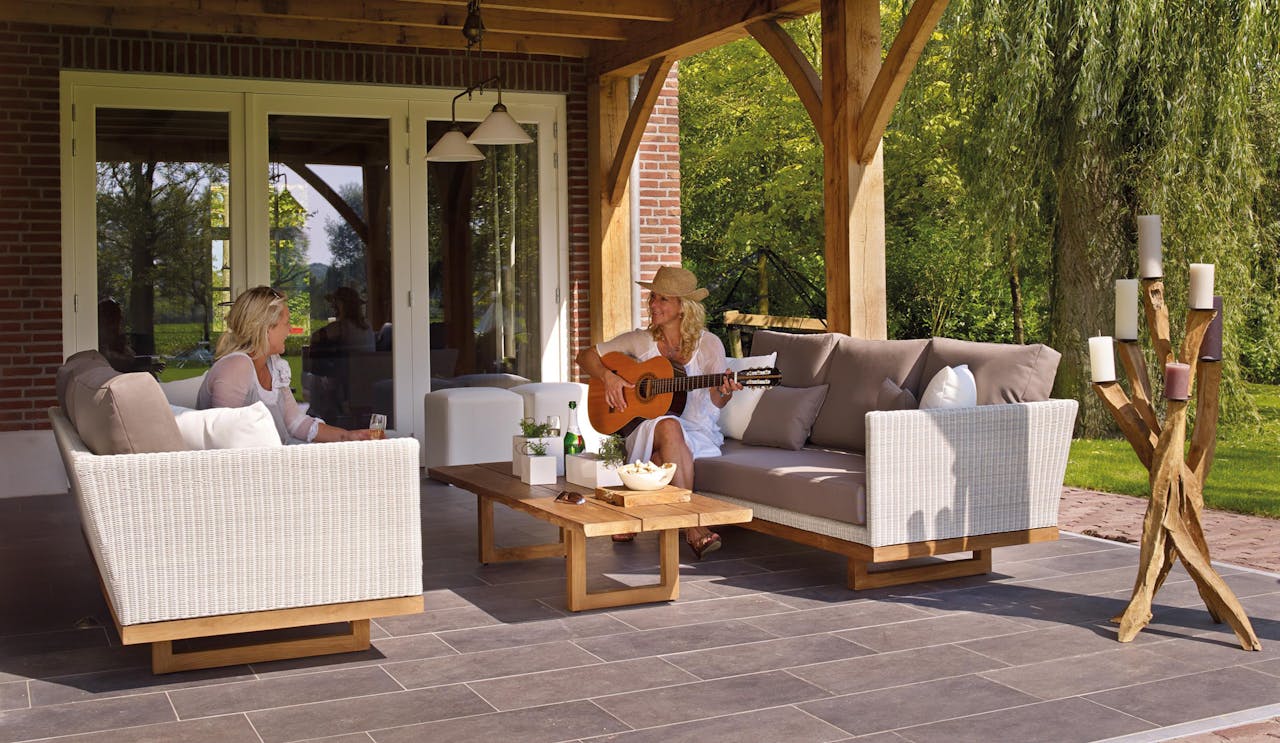 Two people sitting outside on patio furniture while one of them plays the guitar